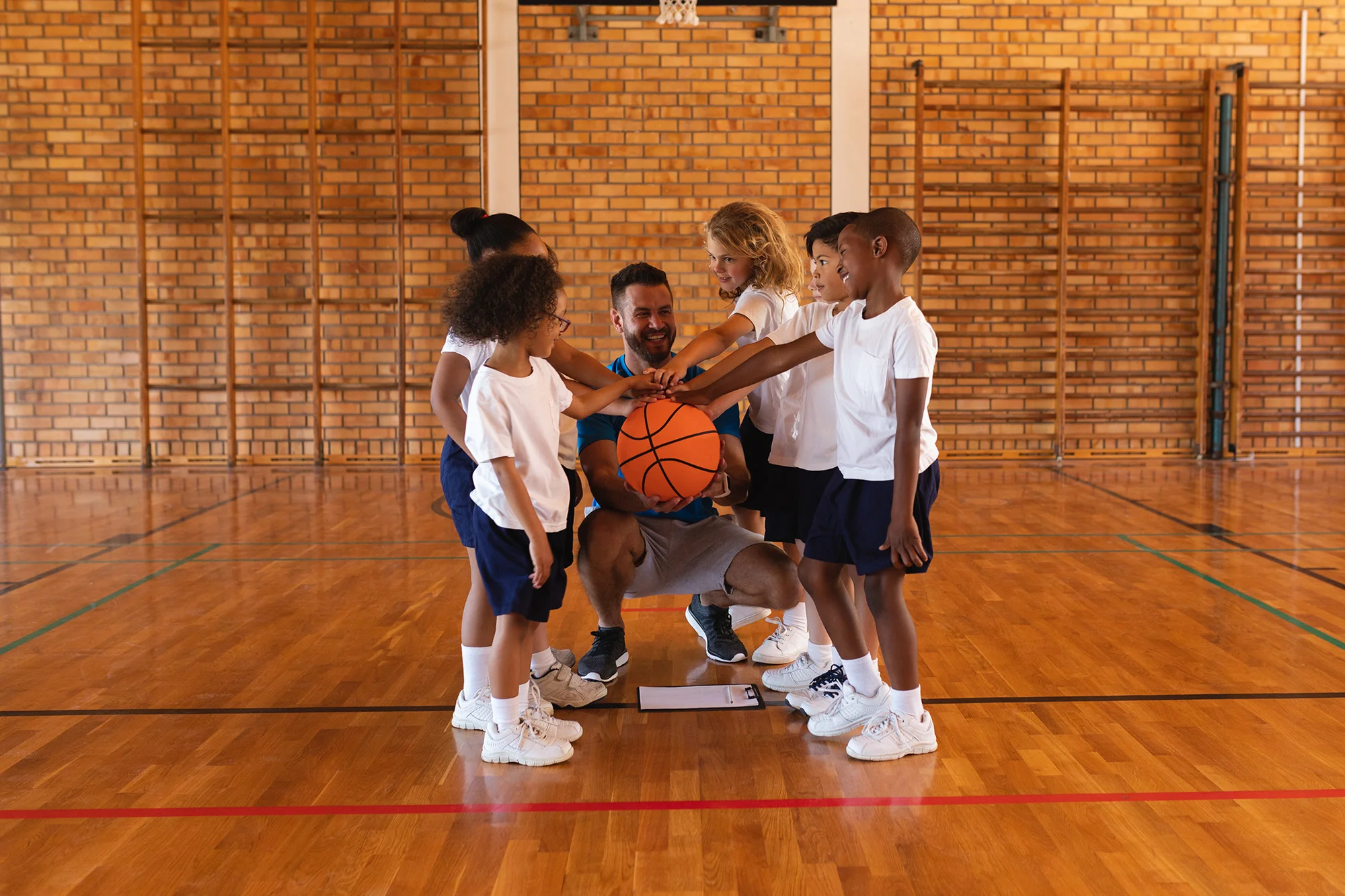 happy schoolkids and basketball coach forming hand