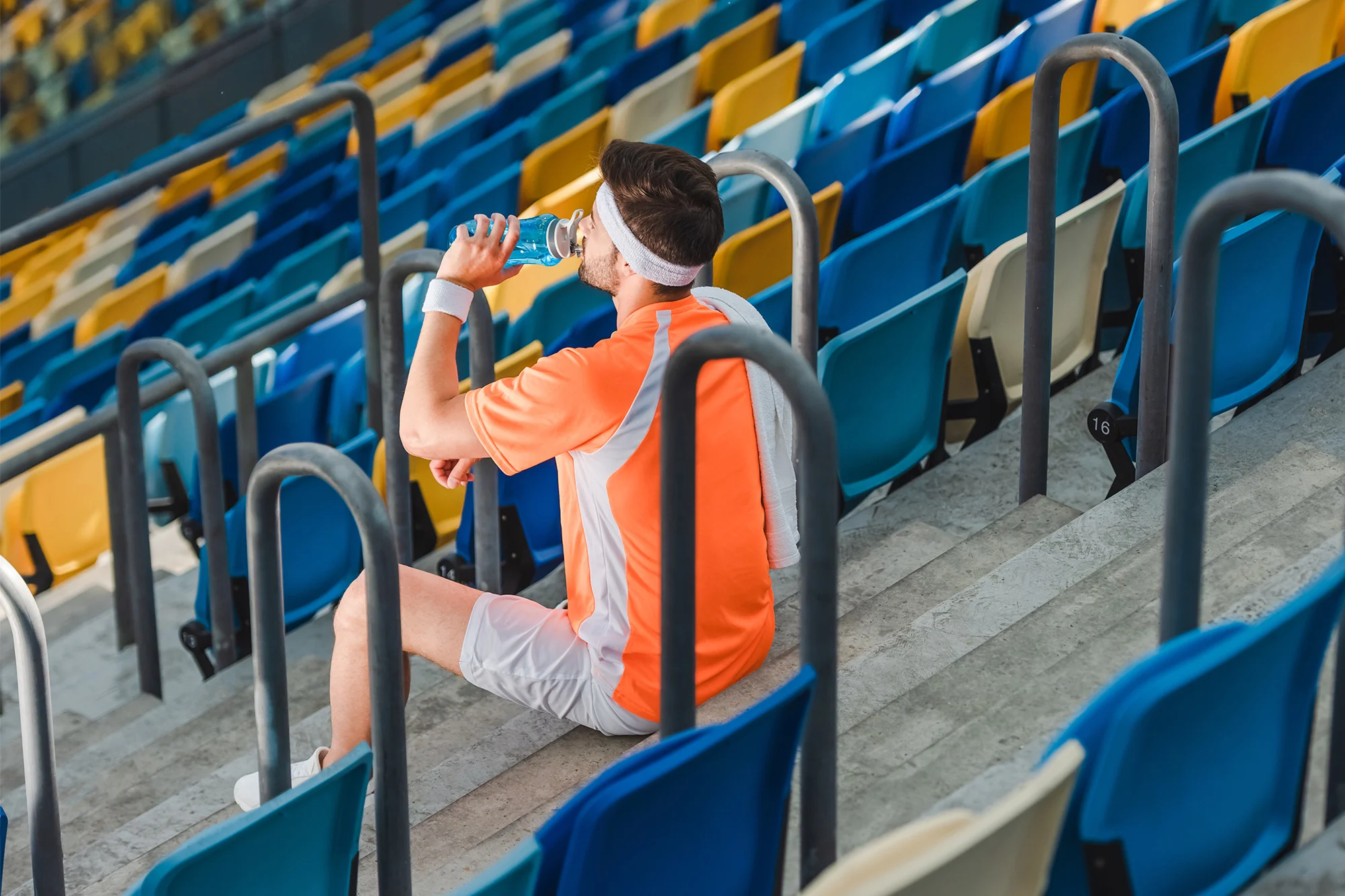 tired young sportsman drinking water while sitting